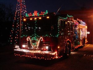 A fire truck decorated with colorful Christmas lights and festive ornaments is parked outside at night, glowing brightly in the darkness.