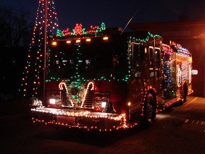 A fire truck decorated with colorful Christmas lights and festive ornaments is parked outside at night, glowing brightly in the darkness.